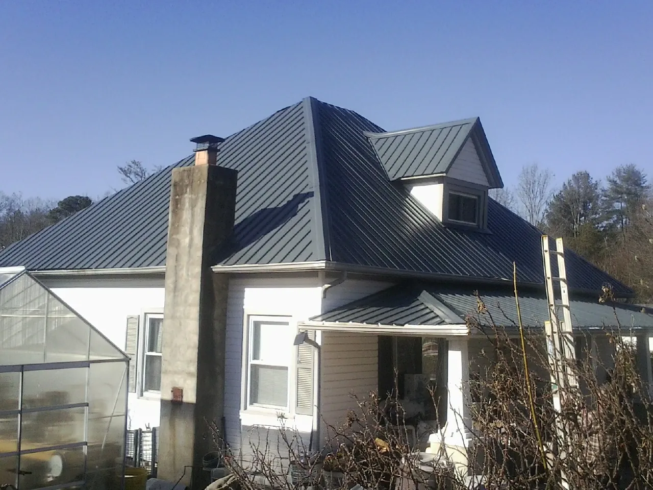Dark blue standing seam metal roof on a white farmhouse with dormer — Slate & Tile Roof Repair by Roofing Brothers in Adrian