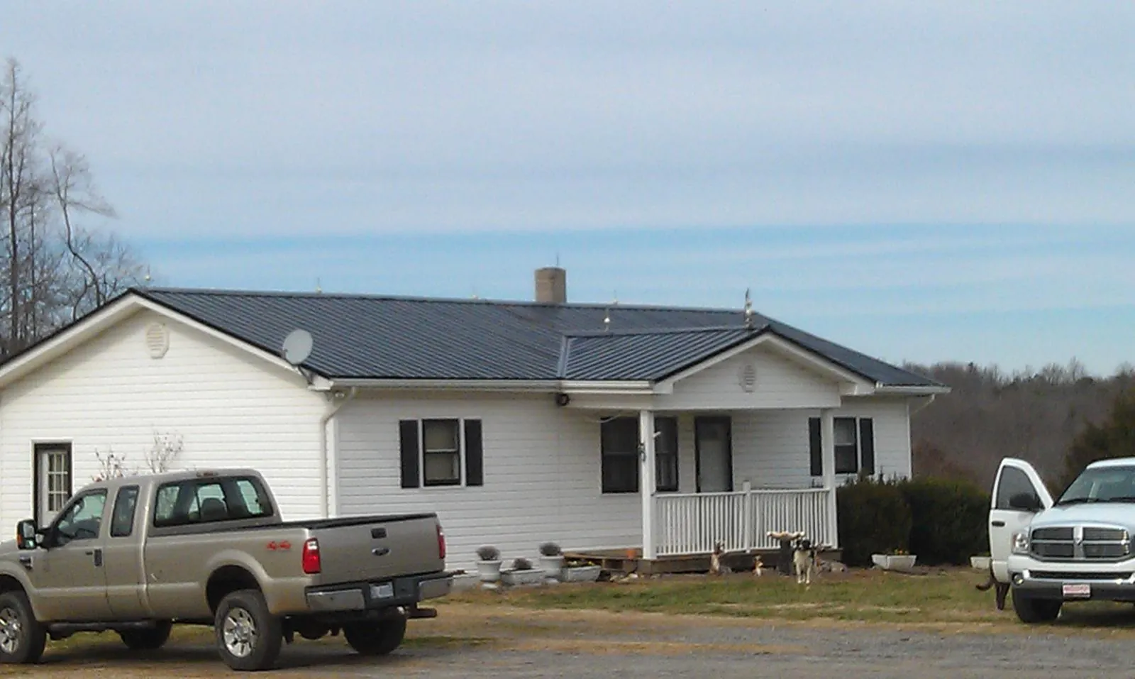 Finished dark metal roof on a white ranch home with work trucks parked in Adrian