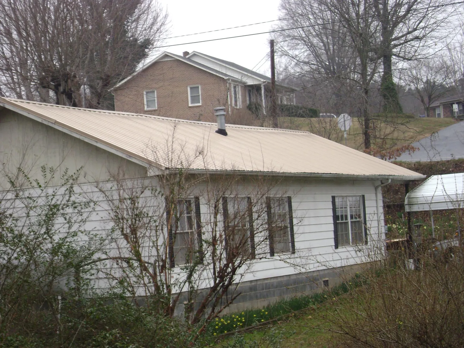 Tan metal roof on a white sided house set into a hillside — Commercial Roofing by Roofing Brothers in Adrian