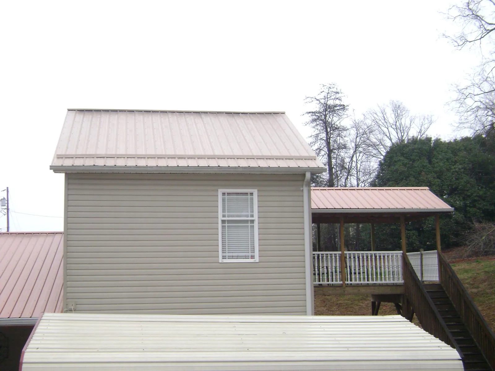 Tan metal roofs on a two story addition and attached porch, from a Roof Replacement job in Adrian